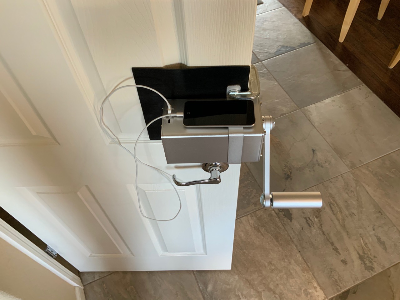The Zeus Dynamo Powerhouse hand crank generator mounted vertically to an indoor door, demonstrating how to fast charge a smartphone.