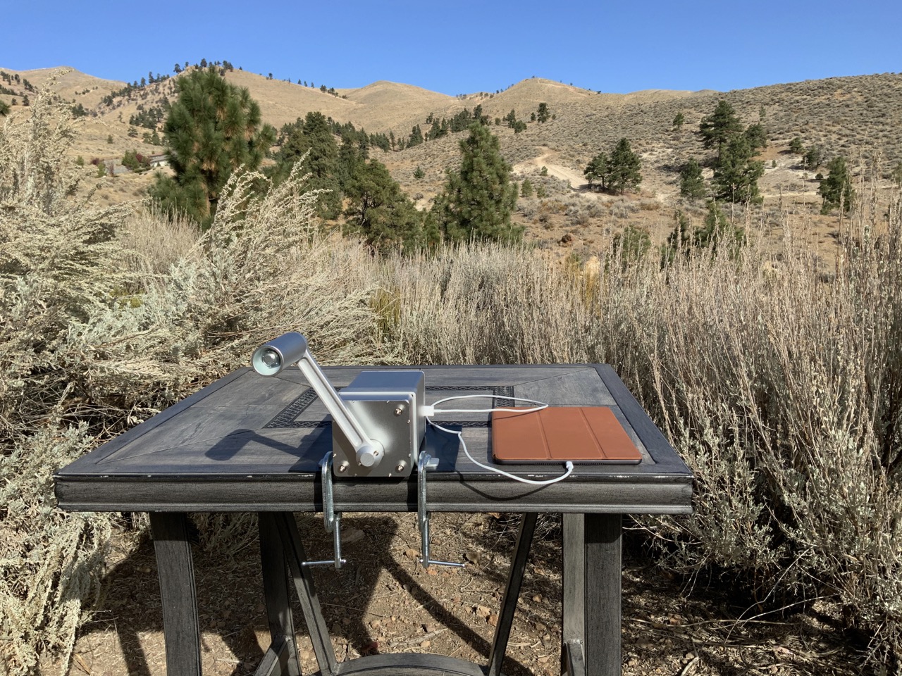 The Zeus Dynamo Powerhouse hand crank generator being used to fast-charge an Apple iPad in a rugged outdoor setting.